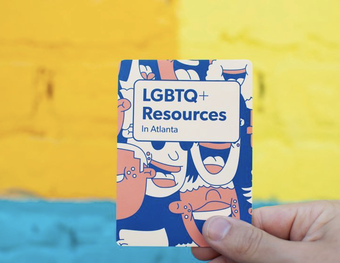Hand holding up LGBTQ+ Resources In Atlanta guide against a colorful painted wall